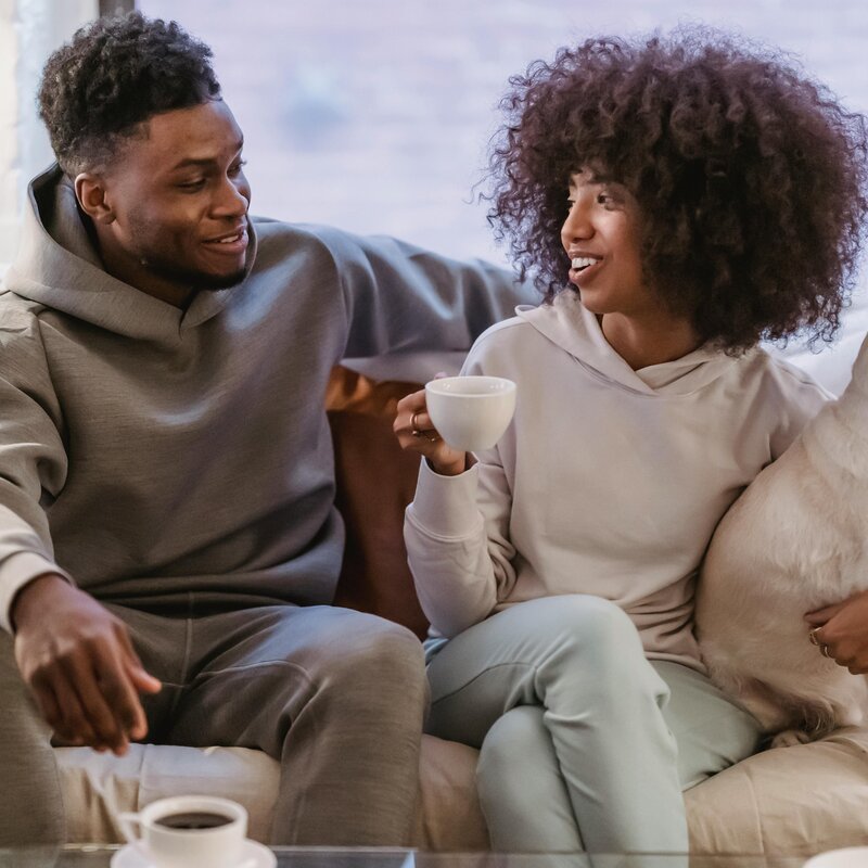 Bild von einem Mann und einer Frau, die auf einer Couch sitzen. Die Frau hat einen Hund im Arm. | © Andres Ayrton | Pexels