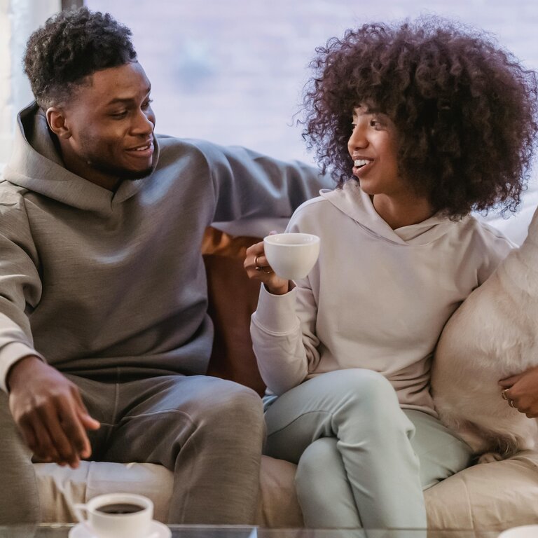 Bild von einem Mann und einer Frau, die auf einer Couch sitzen. Die Frau hat einen Hund im Arm. | © Andres Ayrton | Pexels