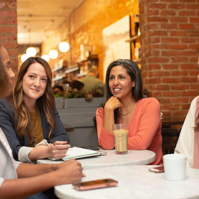 Foto diverser Frauen in einem Meeting, auf dem Tisch stehen Arbeitsmaterialien und Kaffee-Getränke.  | © Unsplash