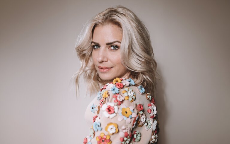 Susan Sideropoulos steht vor einem Fotowand und lächelt | © Liesa Fuchs