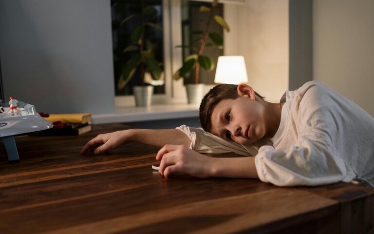 Kind, weißes Hemd, legt kopf traurig auf den Tisch, blickt neutral in die Ferne.  | © Cottonbro | Pexels