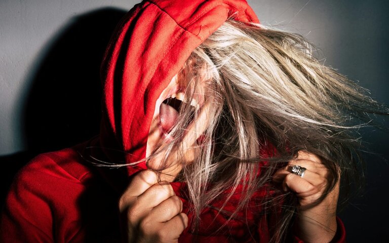 Eine Frau in rotem Kapuzenpulli schreit wütend und ballt sie Hände zu Fäusten. | © Bild: Jan Kopriva | Unsplash