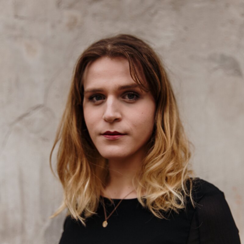 Unsere Werkstudentin Mona in schwarzem Shirt vor einer grauen Betonwand (draußen) | © Foto: Conrad Wegener | EDITION F