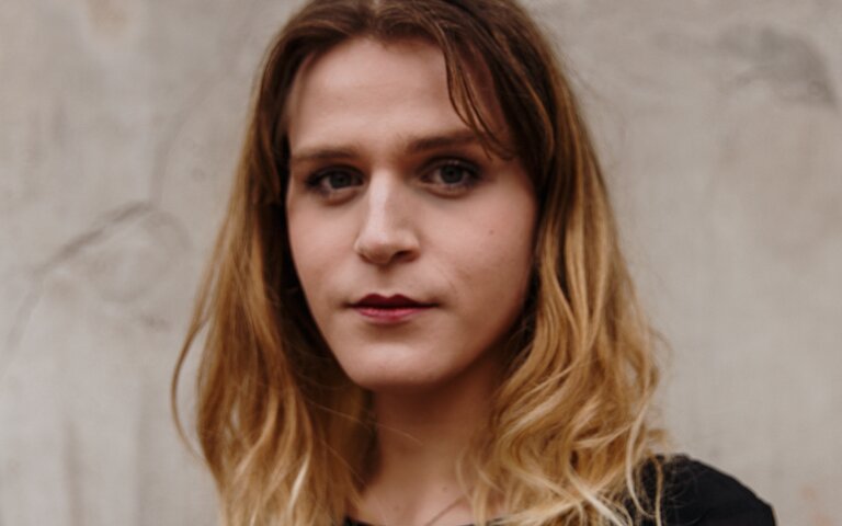 Unsere Werkstudentin Mona in schwarzem Shirt vor einer grauen Betonwand (draußen) | © Foto: Conrad Wegener | EDITION F