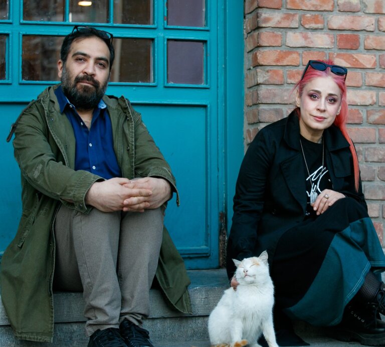 Das Foto zeigt einen Mann und eine Frau, die auf einer Stufe vor eine Tür sitzen. | © Behtash Sanaeeha und Maryam Moghadam |  Foto: Mehdi Hasani 