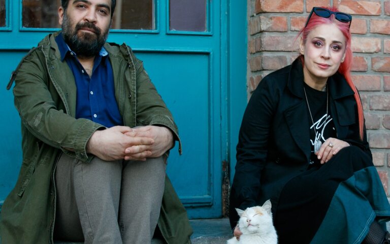 Das Foto zeigt einen Mann und eine Frau, die auf einer Stufe vor eine Tür sitzen. | © Behtash Sanaeeha und Maryam Moghadam |  Foto: Mehdi Hasani 