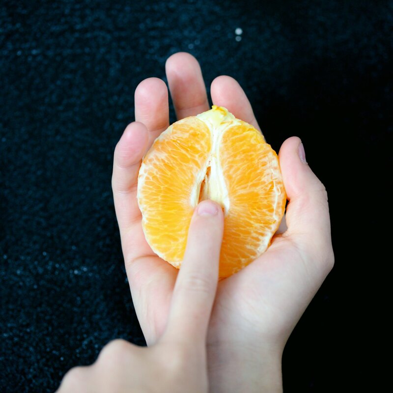 Eine Hand hält eine halbe, geschälte Orange, die eine Vulva symbolisieren soll. | © Foto: Sharon McCutcheon/Unsplash

