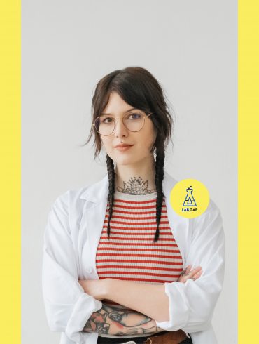 Host des Podcasts Lab Gap, Victoria Müller, trägt einen Laborkittel und blickt selbstbewusst in die Kamera.