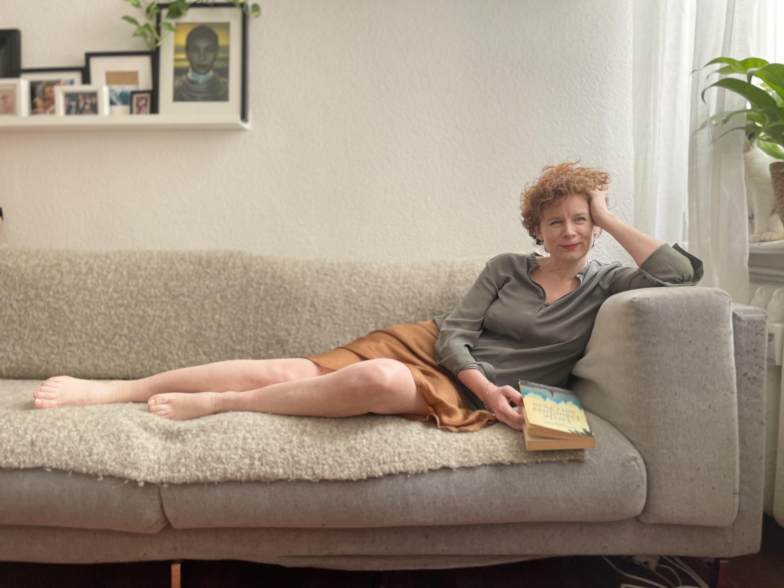 Auf dem Foto ist die Autorin Tina Molin zu sehen, die lächelnd und mit einem Buch in der Hand auf einem Sofa lehnt.
