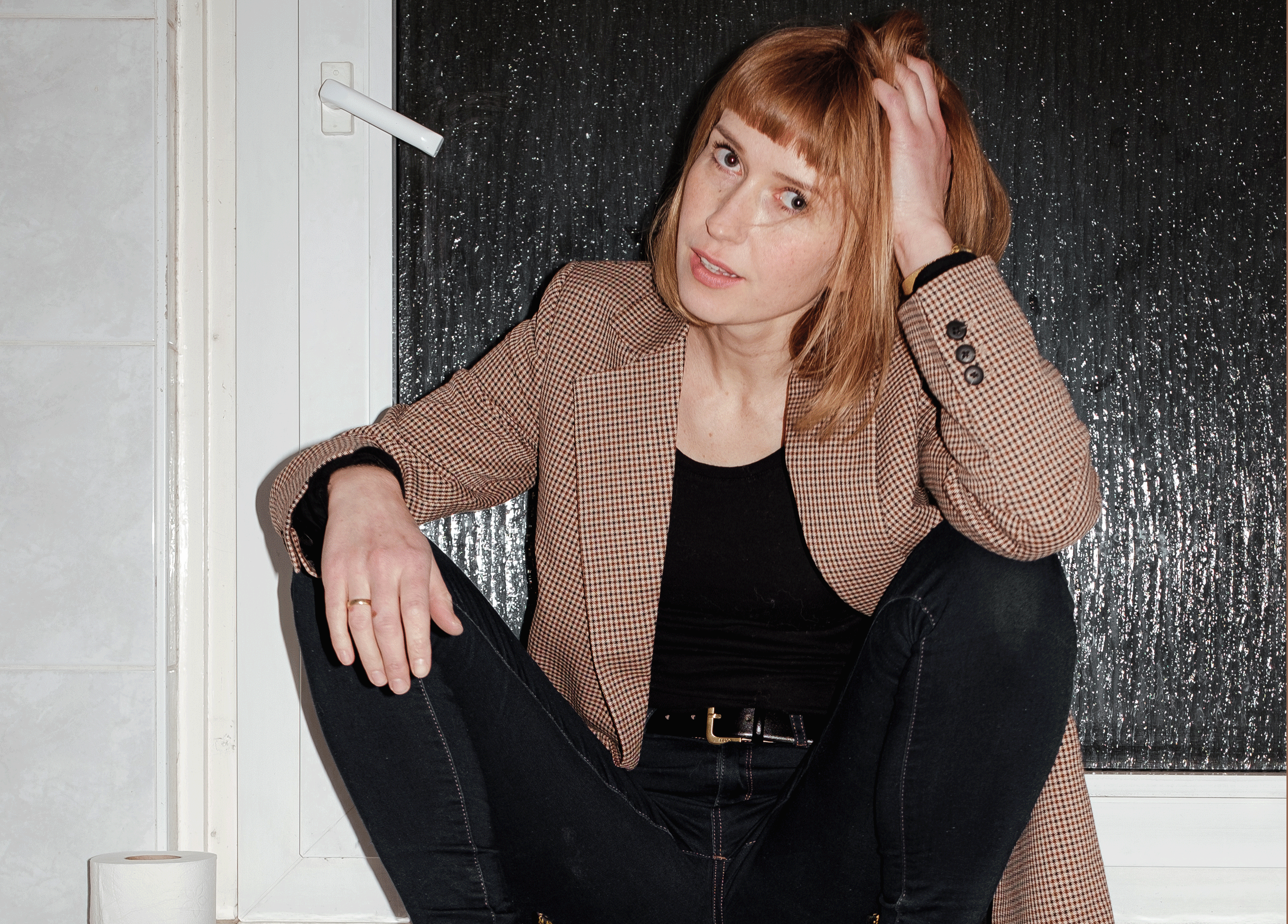 Katja Lewina sitzt mit Schuhen und Jacke auf einer Heizung neben einer Klopapierrolle.