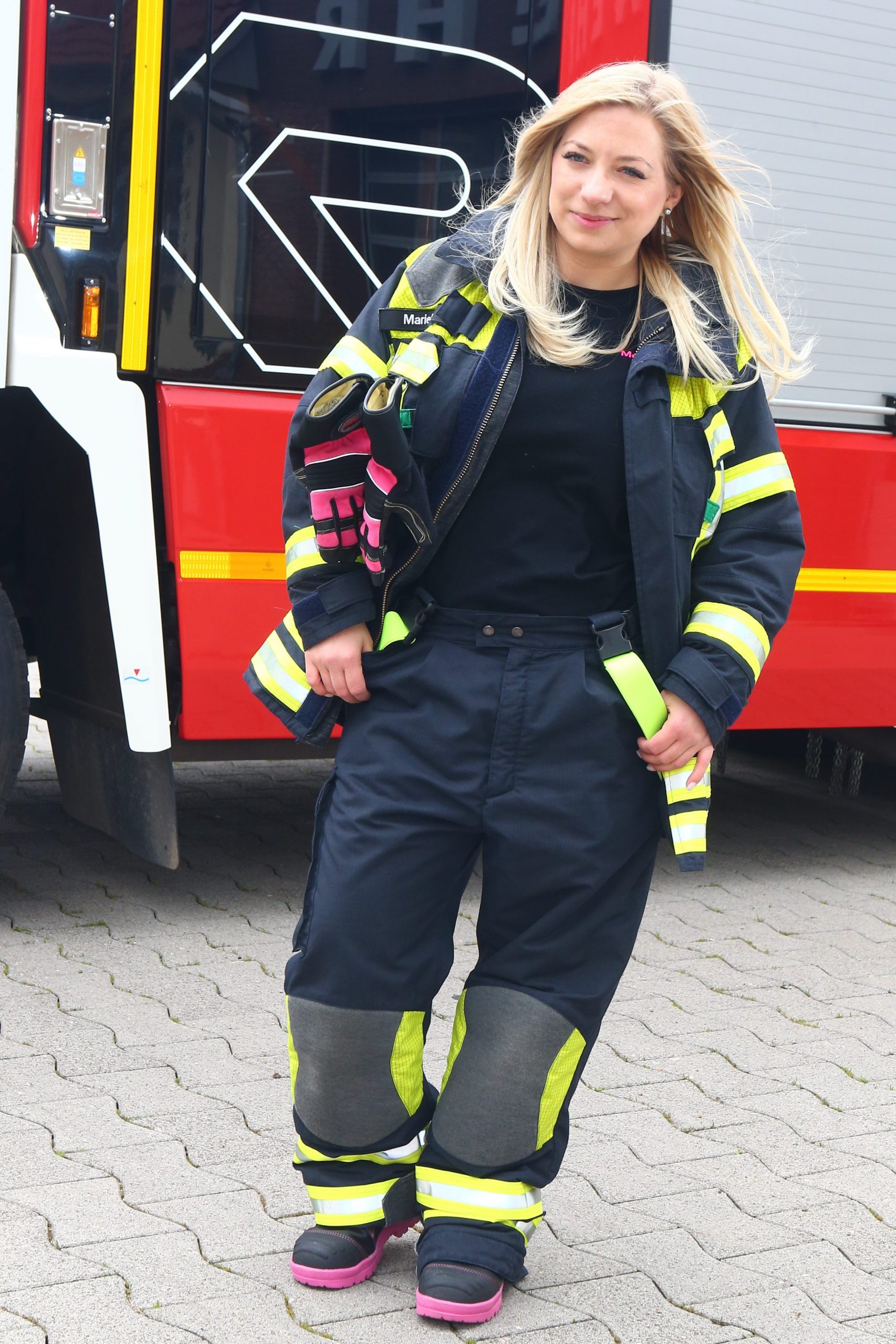 Marie Trappen ist Feuerwehrfrau und steht in voller Montur vor einem Einsatzfahrzeug.