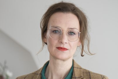 Auf dem Foto ist die Publizistin Franziska Schutzbach zu sehen, sie trägt eine flaschengrüne Bluse und einen karierten Blazer.