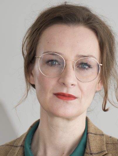 Auf dem Foto ist die Publizistin Franziska Schutzbach zu sehen, sie trägt eine flaschengrüne Bluse und einen karierten Blazer.