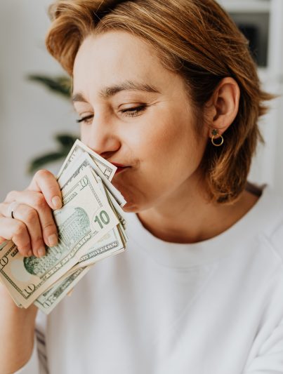 Frau in weißem Shirt hält ein Bündel Geldscheine in Händen.