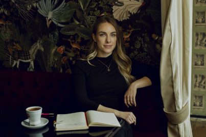 Protagonistin Gina Cohrs sitzt mit Kaffee und Buch in einem Café.
