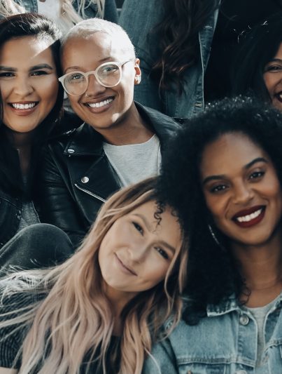 Fünf Frauen, die auf einer Treppe sitzen und lachen und zuversichtlich in die Zukunft blicken.