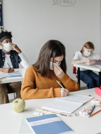 In einem Klassenzimmer: Drei Kinder sitzen einzeln an Tischen und tragen eine Gesichtsmaske, um die Ansteckung von Covid vorzubeugen.
