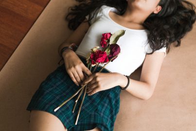 Frau liegt mit verwelkten Rosen auf einem Bett