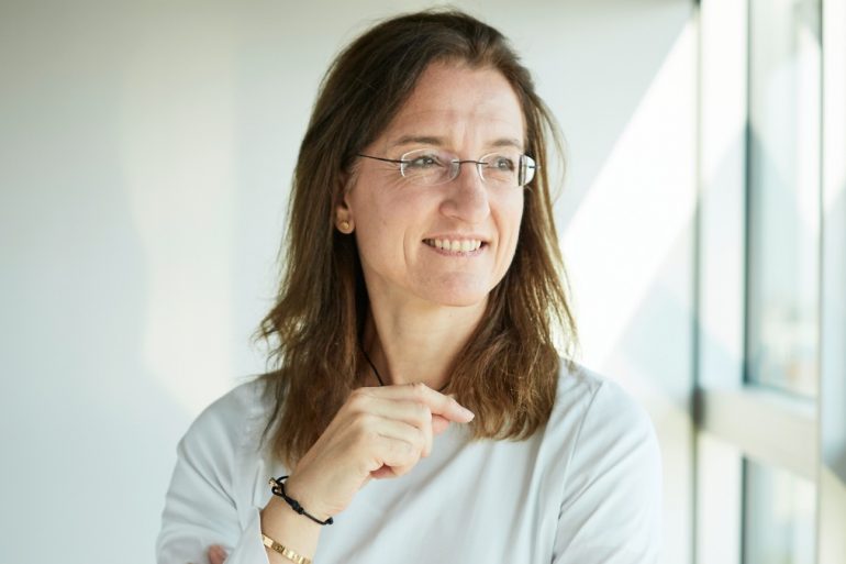 Kerstin Wagner, HR-Chefin der Deutschen Bahn, weißes Oberteil vor weißem Hintergrund, blickt schräg links an Kamera vorbei aus dem Fenster. Sie trägt eine Brille und braunes Haar.