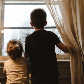 Zwei Kinder warten am Fenster auf die Eltern.