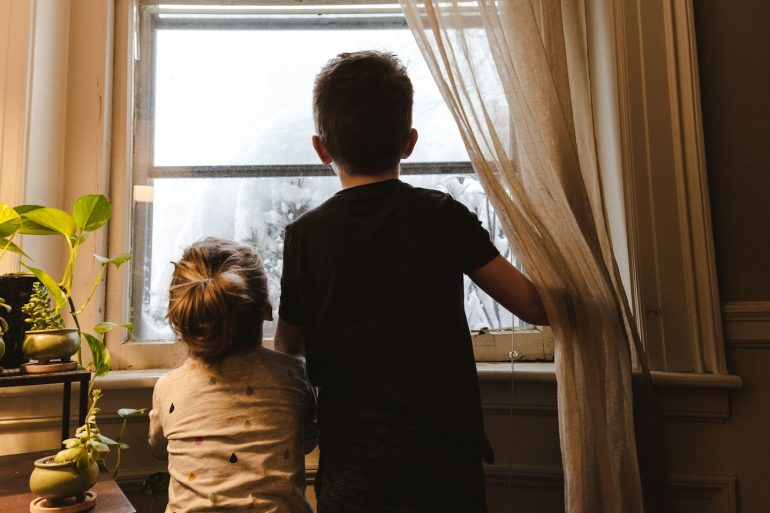 Zwei Kinder warten am Fenster auf die Eltern.