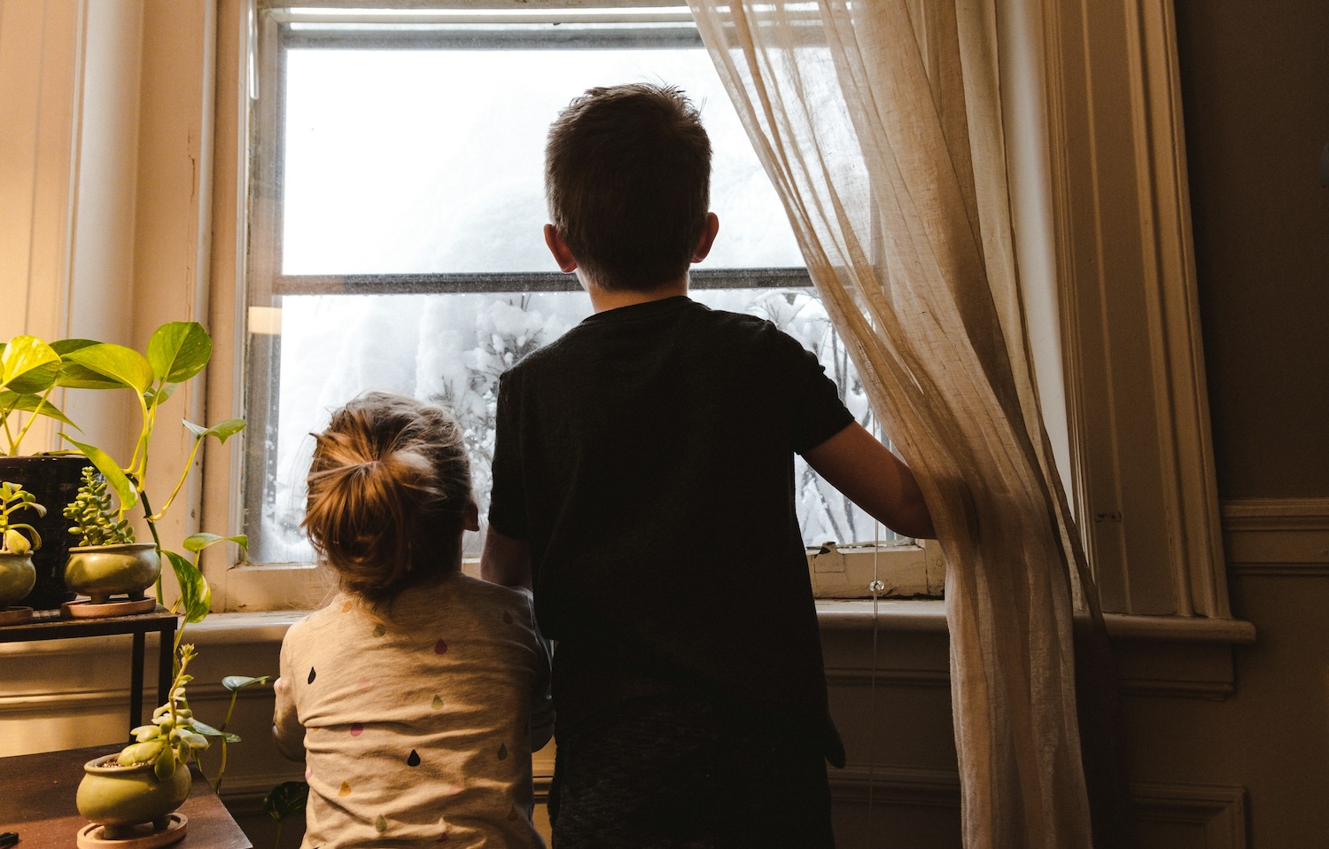 Zwei Kinder warten am Fenster auf die Eltern.