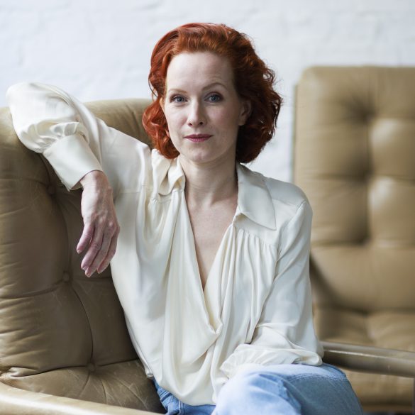 Teresa Bücker in weißer Bluse und in hellblauen Jeans, sitzend auf einem beigen Lesersessel, Blick in die Kamera.
