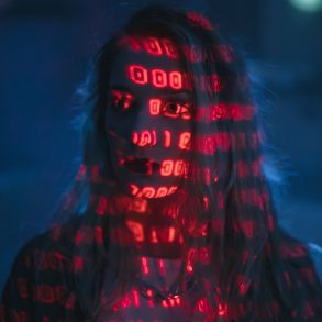 Frau im rötlichen Schatten, auf ihr sind digitale Codes zu sehen, Person als Projektionsfläche