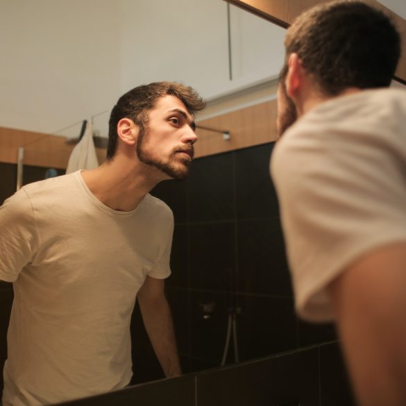 Mann in weißem Shirt, der sich im Spiegel anschaut.