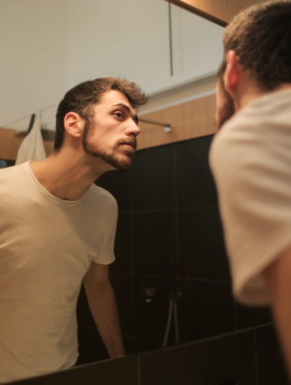 Mann in weißem Shirt, der sich im Spiegel anschaut.