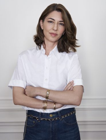Das Bild zeigt die Regisseurin Sofia Coppola vor einer weißen Wand stehend.