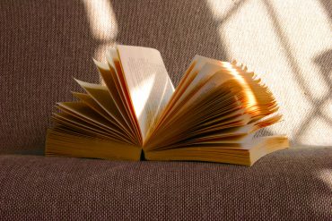 Ein Buch liegt aufgeschlagen auf einem Sofa in der Sonne.