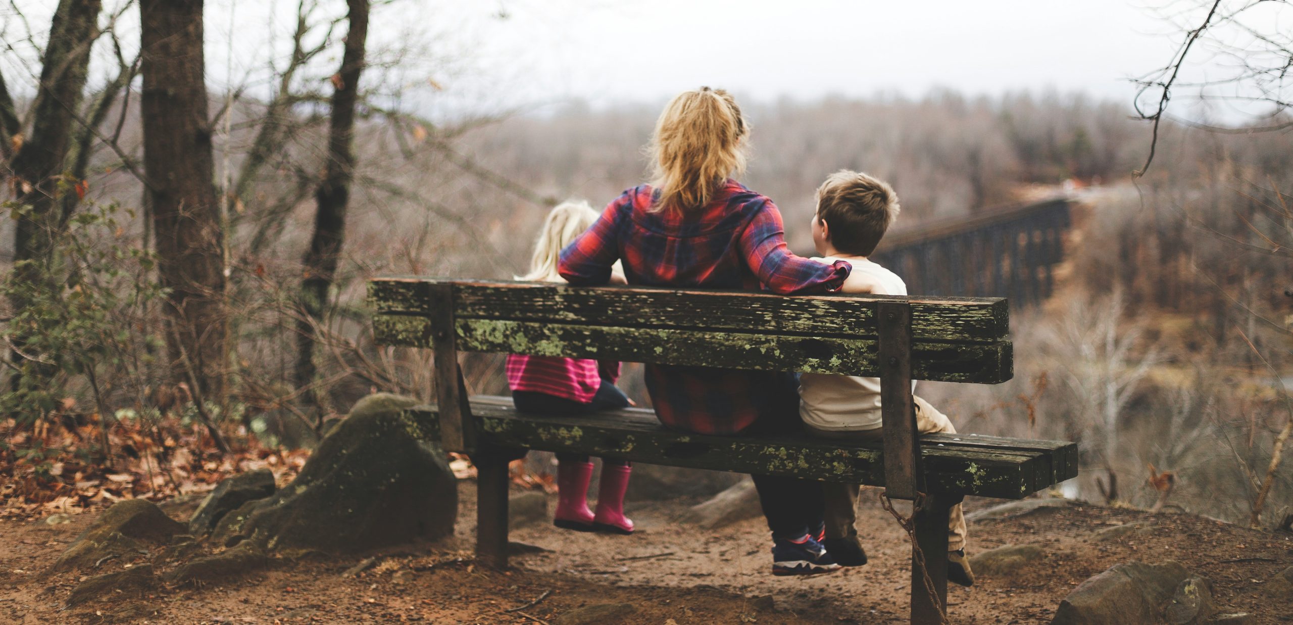 Eine Frau sitzt mit zwei kleinen Kindern auf einer Bank und schaut in die Natur.