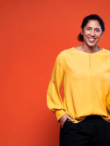 Bild von Steffi Jones in gelber Bluse mit einem gelben Ball vor rotem Hintergrund