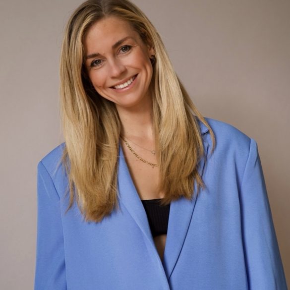 Lara Sophie Bothur in einem hellblauten Blazer im Porträt, blonde lange Haare, sie legt den Kopf leicht schief und lächelt in die Kamera.