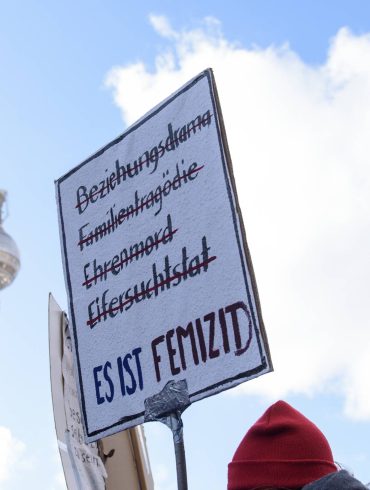 Demonstrationsschild: Es ist Femizid. Hintergrund: Blauter Himmel und Fernsehturm in Berlin