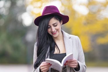 Frau mit rotem Hut und schwarzen langen Haaren liest ein Buch im Herbst.