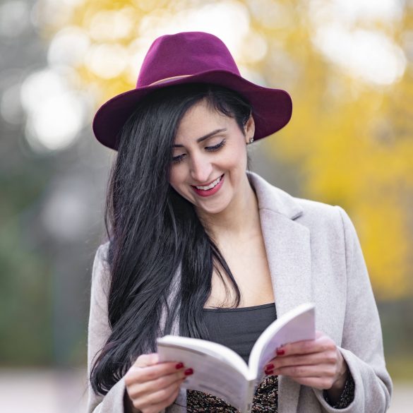 Frau mit rotem Hut und schwarzen langen Haaren liest ein Buch im Herbst.