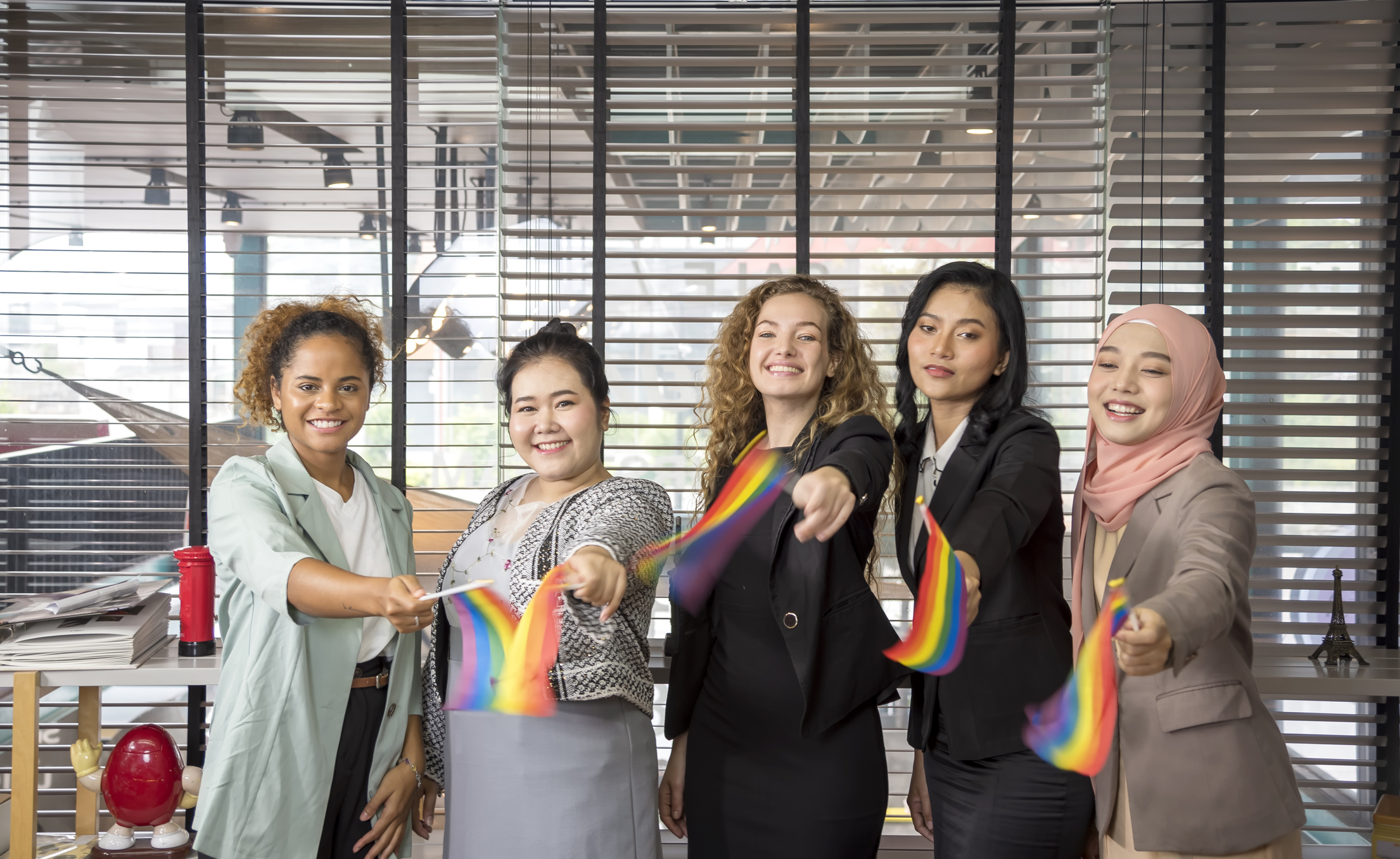 Fünf Menschen stehen nebeneinander, lächeln und halten Regenbogenfahnen in den Händen