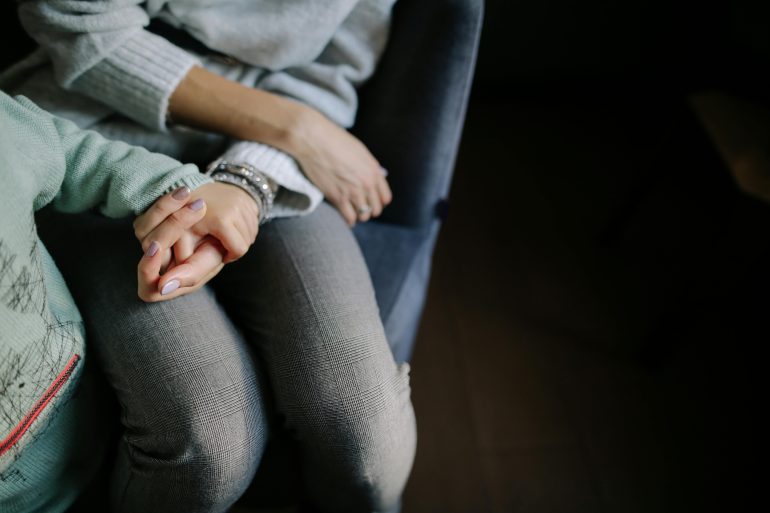 Frau und Kind sitzen nebeneinander, wartend. Man sieht ihre Gesichter nicht.