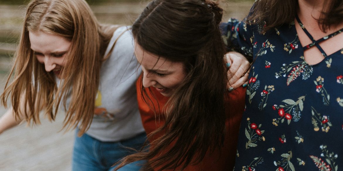 Drei Frauen halten einander fest und lachen.