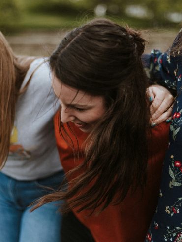 Drei Frauen halten einander fest und lachen.