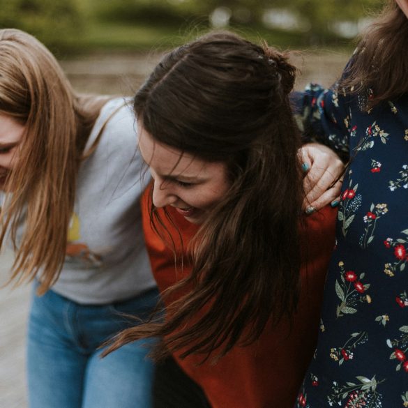 Drei Frauen halten einander fest und lachen.