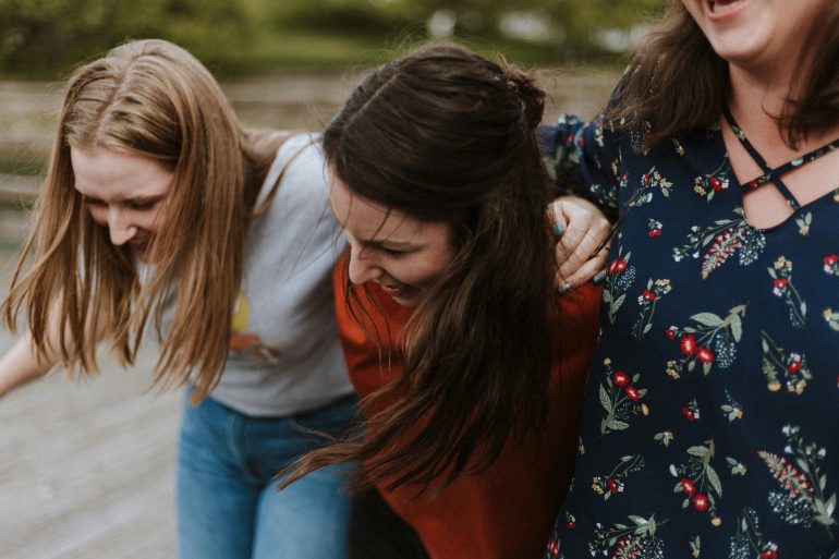 Drei Frauen halten einander fest und lachen.