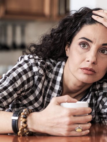 Eine Frau sitzt am Tisch und hält sich den Kopf.