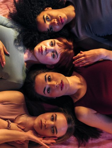 Bild von vier Frauen, die eng nebeneinander auf einer Decke liegen.