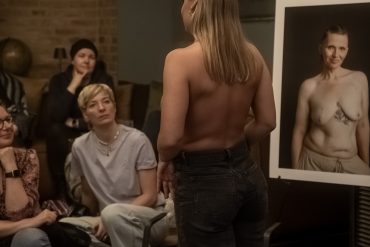Eine Frau zeigt ihre Brustkrebsnarbe. Rundherum stehen Bilder von Frauen, die ihre Narben fotografieren ließen.
