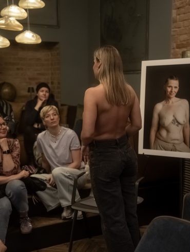 Eine Frau zeigt ihre Brustkrebsnarbe. Rundherum stehen Bilder von Frauen, die ihre Narben fotografieren ließen.